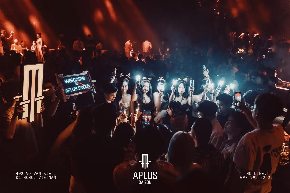 APLUS MUSIC SAIGON 现场 · 人群举着发光灯棒，前排抬着写有 welcome to APLUS SAIGON 的 LED 灯牌与 A 字灯箱