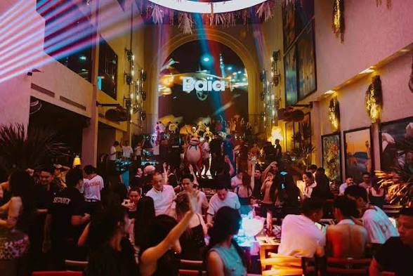 BAIA SAIGON 侧翼长桌卡座坐满客人，远处拱门大屏亮着 Baia 字样