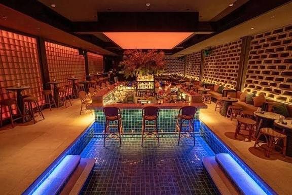 BAM BAR 中央水池吧台：环形吧台立在浅水池中央，池底蓝色灯带、四周玻璃砖墙与顶部橙粉色发光天花