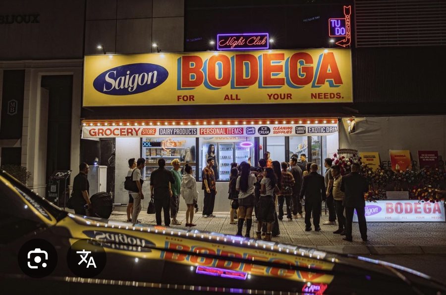 BODEGA SAIGON 门头夜景：黄底 Saigon BODEGA 杂货店招牌、Night Club 粉色霓虹与 TU DO DANCING 竖排红霓虹，门口聚着排队的客人