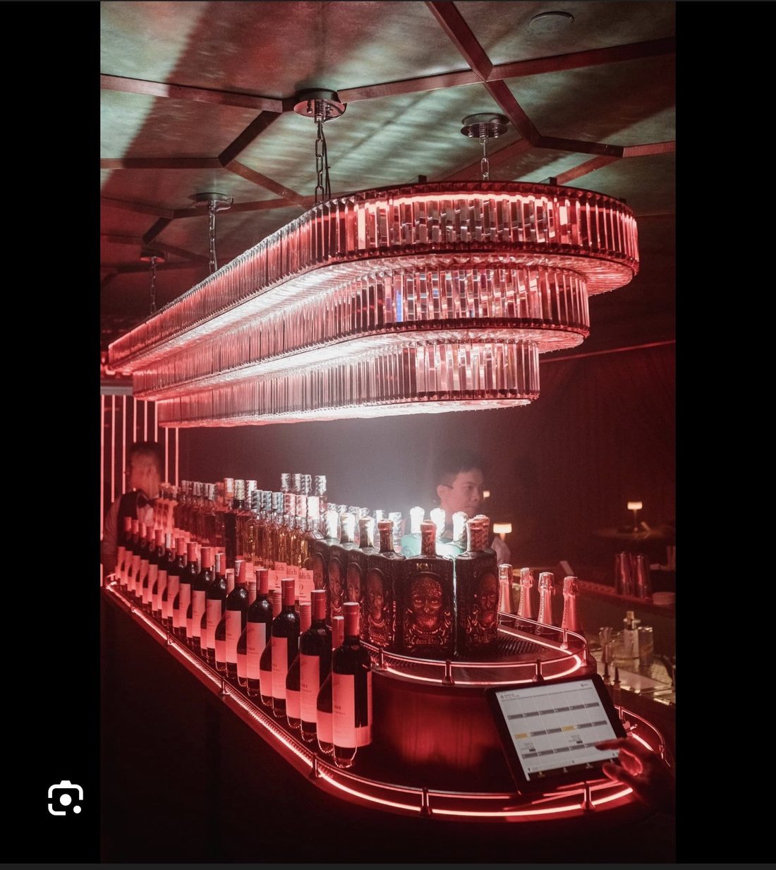 BODEGA SAIGON 吧台:三层长条水晶吊灯下的整排洋酒与气泡酒,红色灯带勾出弧形台沿