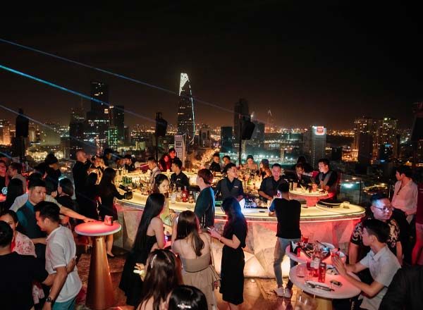 CHILL SKY BAR 夜晚人群围着中央吧台,远处西贡高楼群与 Bitexco 塔尖