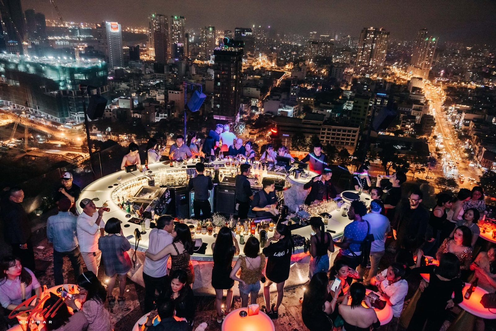 CHILL SKY BAR 胡志明第一郡 26 楼露天天台，中央发光环形吧台被人群围满，背后是整片西贡夜景与车流