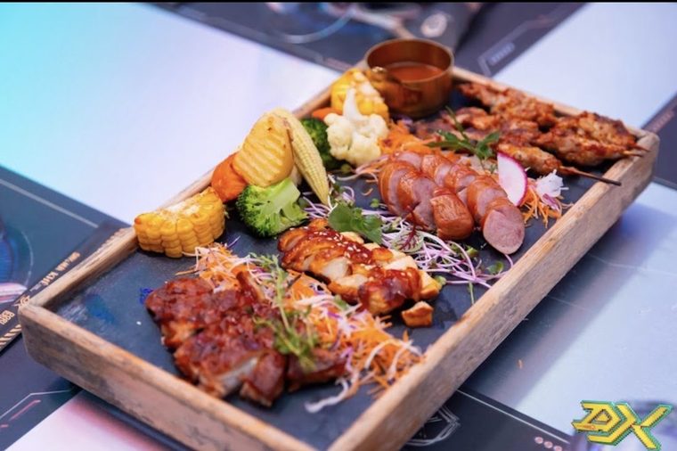 DISTRICT K 韩式烤肉拼盘:梅花肉、酱烧鸡腿、香肠切片、串烧配烤玉米与西兰花,摆在发光的赛博纹台面上