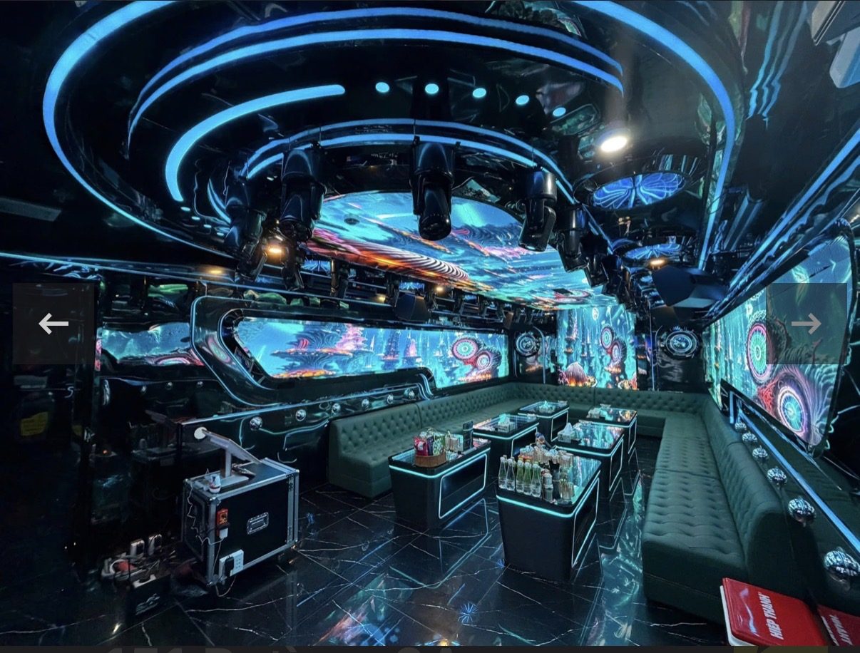 DRAGON PALACE 龙宫 KTV 大包厢，天花做同心圆蓝色光环并挂一排摇头灯，四面 LED 屏放深海珊瑚画面，墨绿绒面钮扣卡座围成大圈