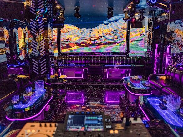 大房 DJ 舱:前景一整套 DJ 打碟控制台,正墙弧形 LED 放彩色山脉,两侧人字纹发光墙板