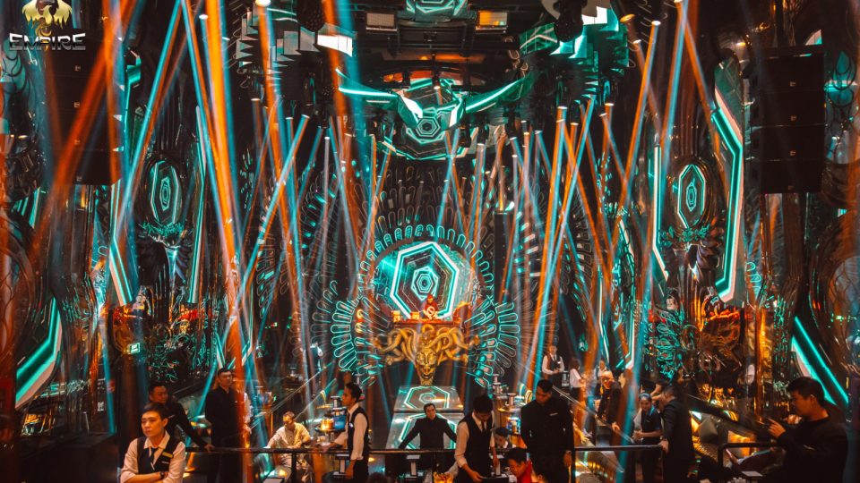 EMPIRE MUSIC BAR 蓝绿色灯光时段:整面巴洛克科技风 LED 墙、中央金色羊首徽章与扇形霓虹光环,几十道激光从穹顶交叉射下