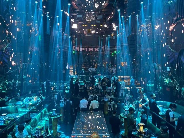 EMPIRE MUSIC BAR 二层视角:蓝色激光垂落,后墙 EMPIRE 灯字亮着,中央发光走秀台两侧是阶梯式卡座