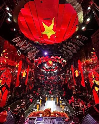EMPIRE MUSIC BAR 从 DJ 台后方看全场:环形 LED 穹顶整块显示越南国旗红底黄星,两侧红色 LED 墙铺满花卉纹样,中央走秀台上有龙形道具