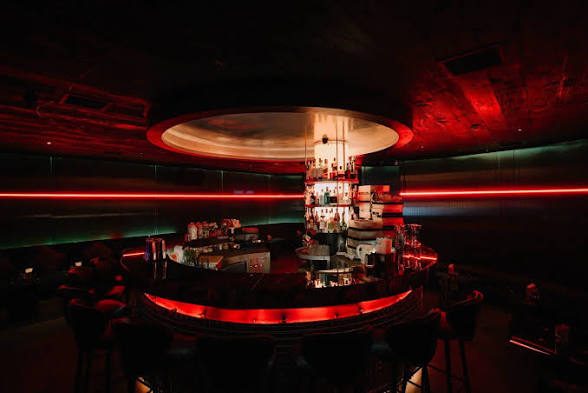 FETTI BAR 圆形中央吧台，酒架立在正中，吧台下沿一道红色 LED，头顶悬着椭圆灯膜