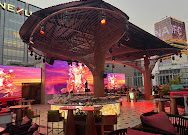 KÉN SKYBAR 傍晚时段：天光未暗，伞状雕塑与粉红色大屏已亮起，露天卡座沿栏杆排开