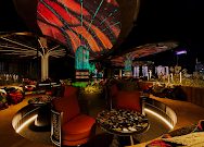 KÉN SKYBAR 胡志明第一郡天台酒吧夜景：波浪状发光顶棚、环形吧台与橘色弧形卡座，背景是城市灯火