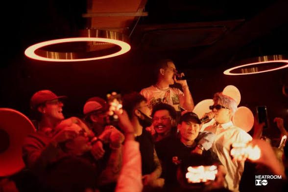 LOCO HEATROOM BAR 现场，戴帽子的 MC 手持麦克风，红色光圈灯下人群举杯