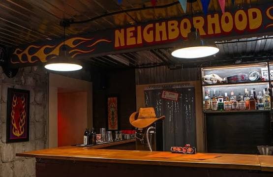 NEIGHBORHOOD BAR 手绘火焰字招牌与木天花吧台，墙上挂牛仔帽与霓虹画框