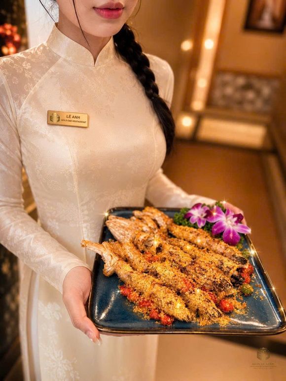 GOLD ONE 餐厅服务人员身着白色奥黛制服、佩戴餐厅金色名牌,端上一盘蒜香大头虾