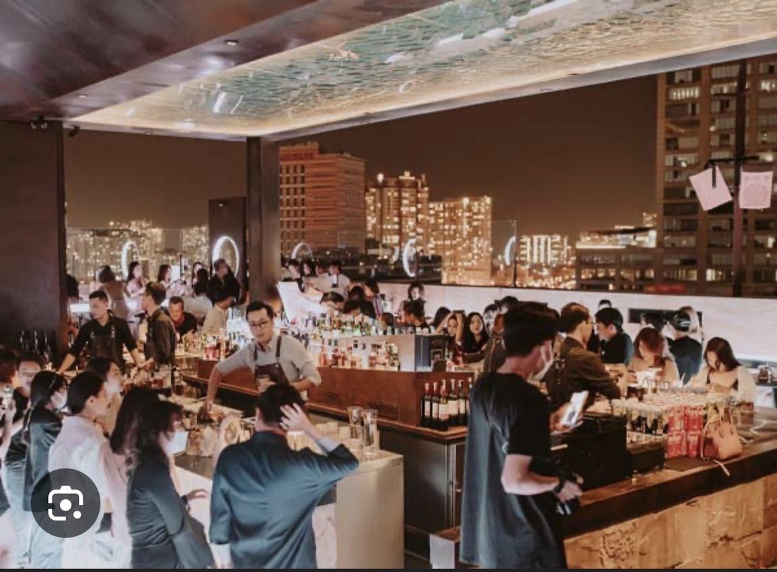 ZION 室内长吧台前站满客人,头顶波纹镜面天花,窗外是胡志明夜景