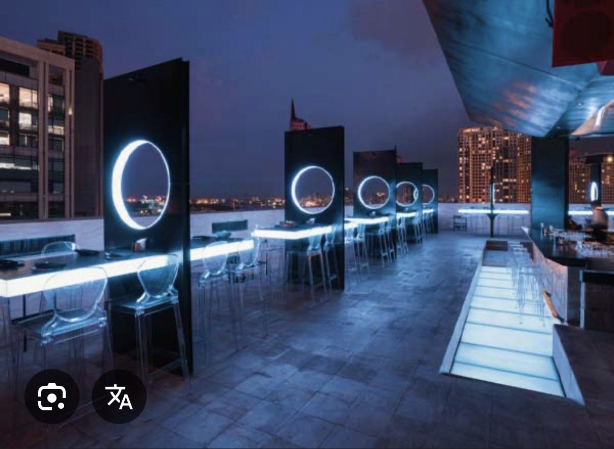 ZION SKY LOUNGE 露台：黑色隔屏上的发光白色圆环、自带灯的长桌与透明亚克力高脚椅，背景是胡志明夜景